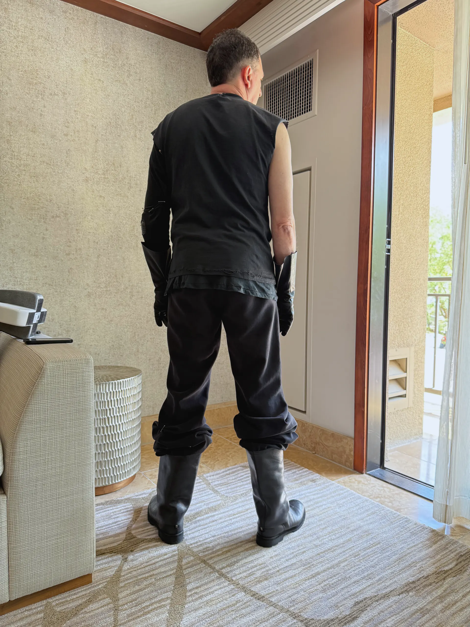 Back view of the same black sleeveless top, long leather gloves, black trousers and tall leather boots