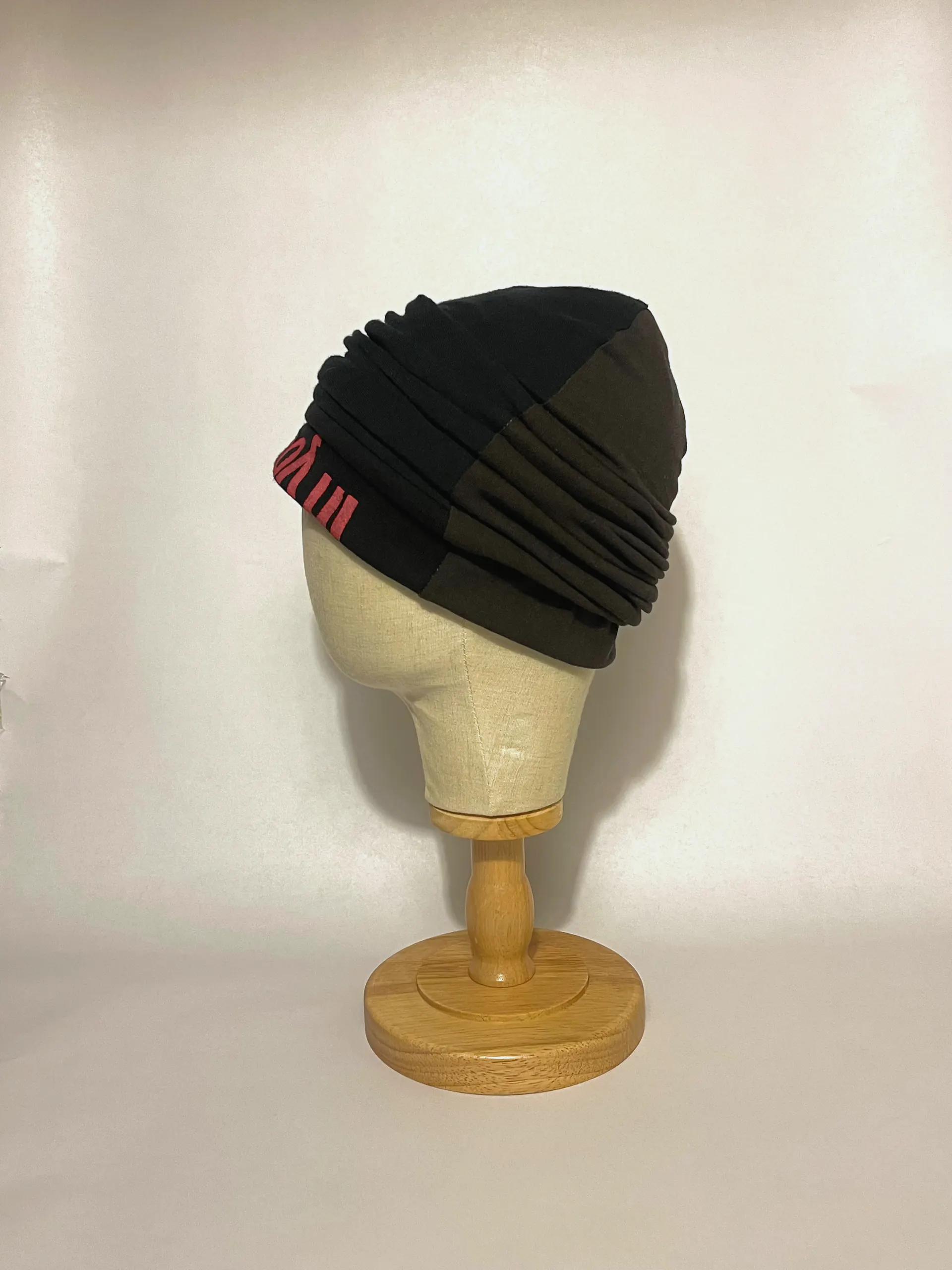 Black pleated jersey head wrap on a linen head form, three-quarter view