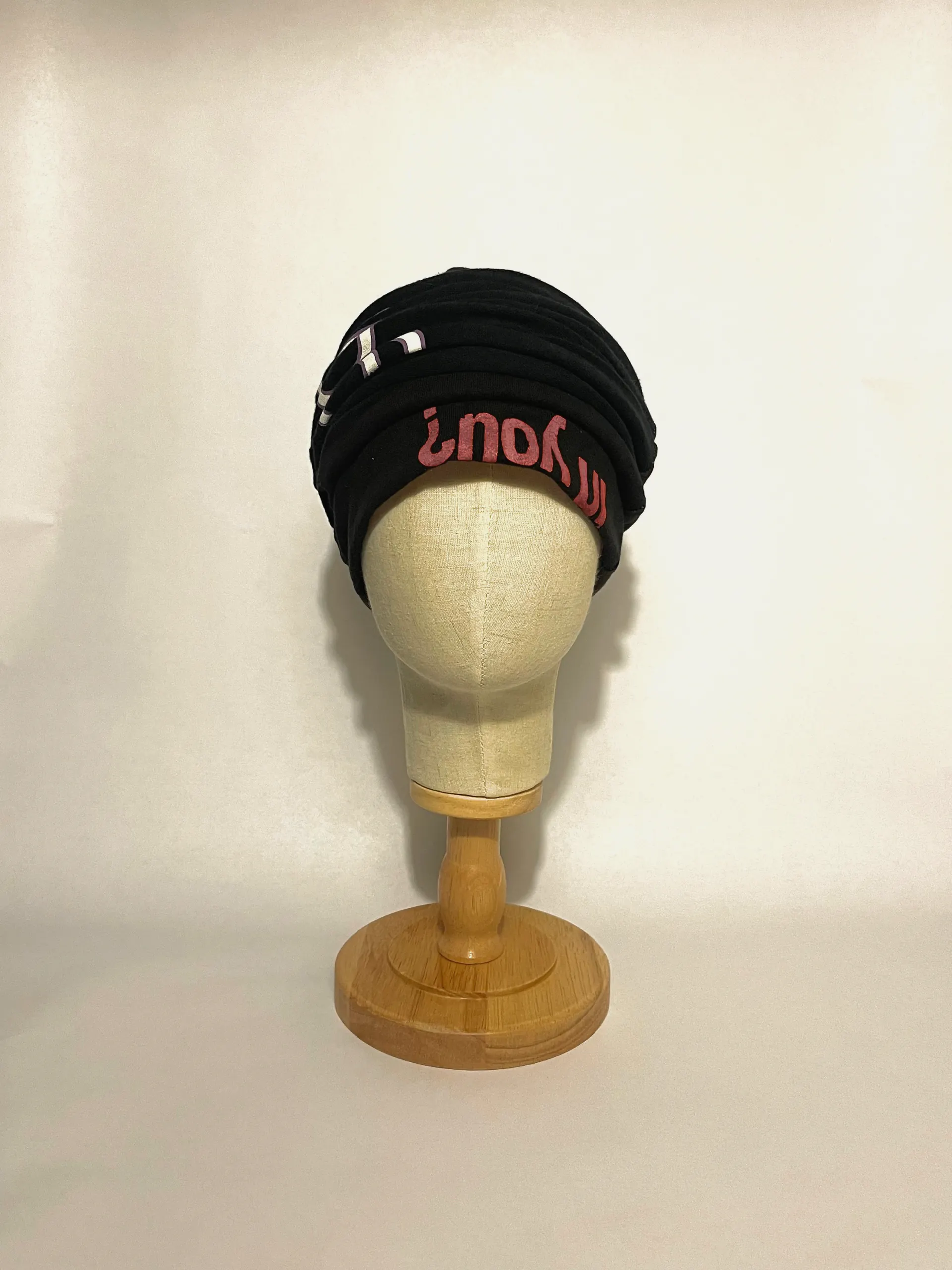 Black pleated jersey head wrap on a linen head form, front view