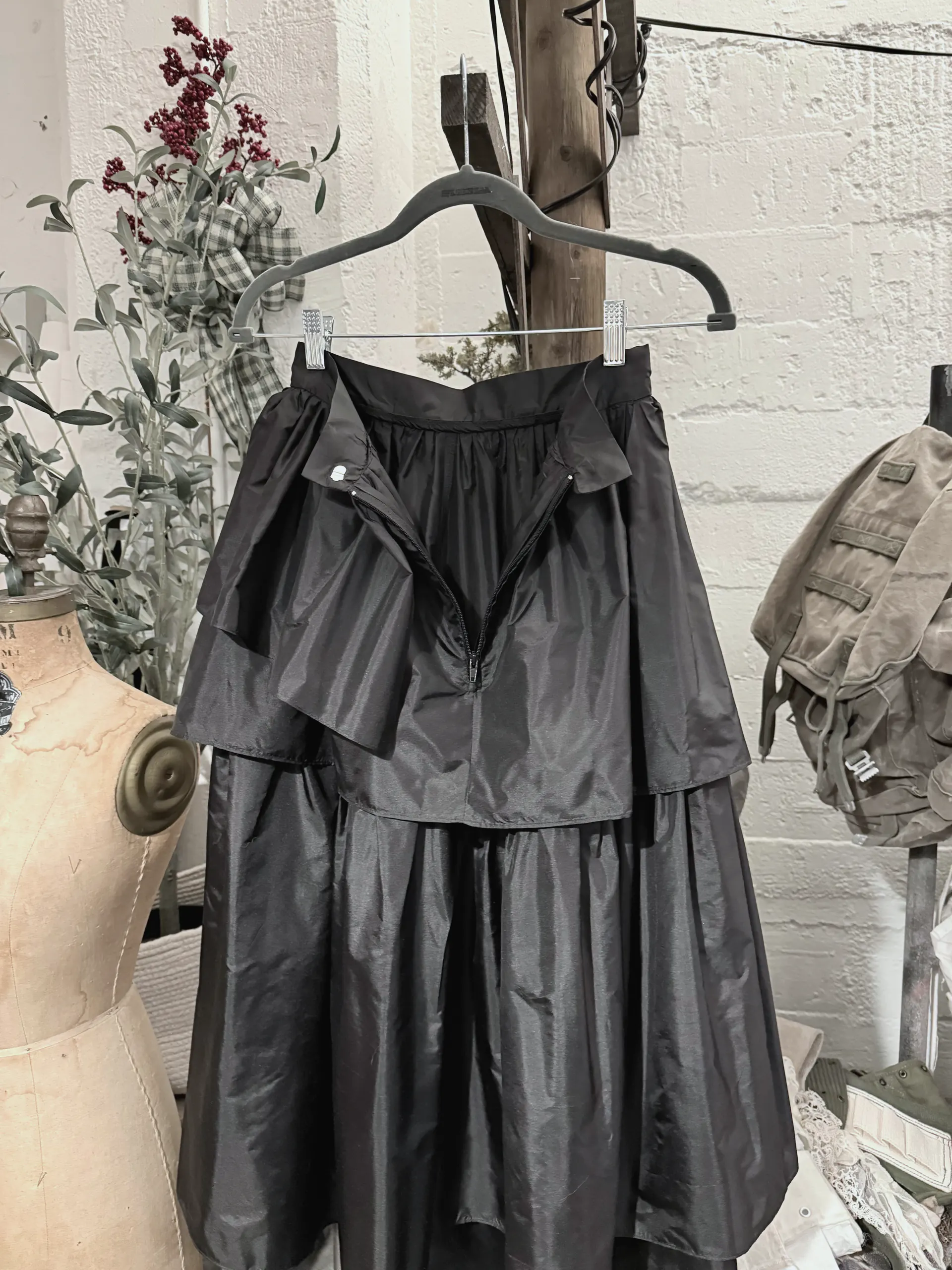 Black tiered taffeta skirt on a hanger, closer view showing the waistband, the open centre-back zip and the top tier.